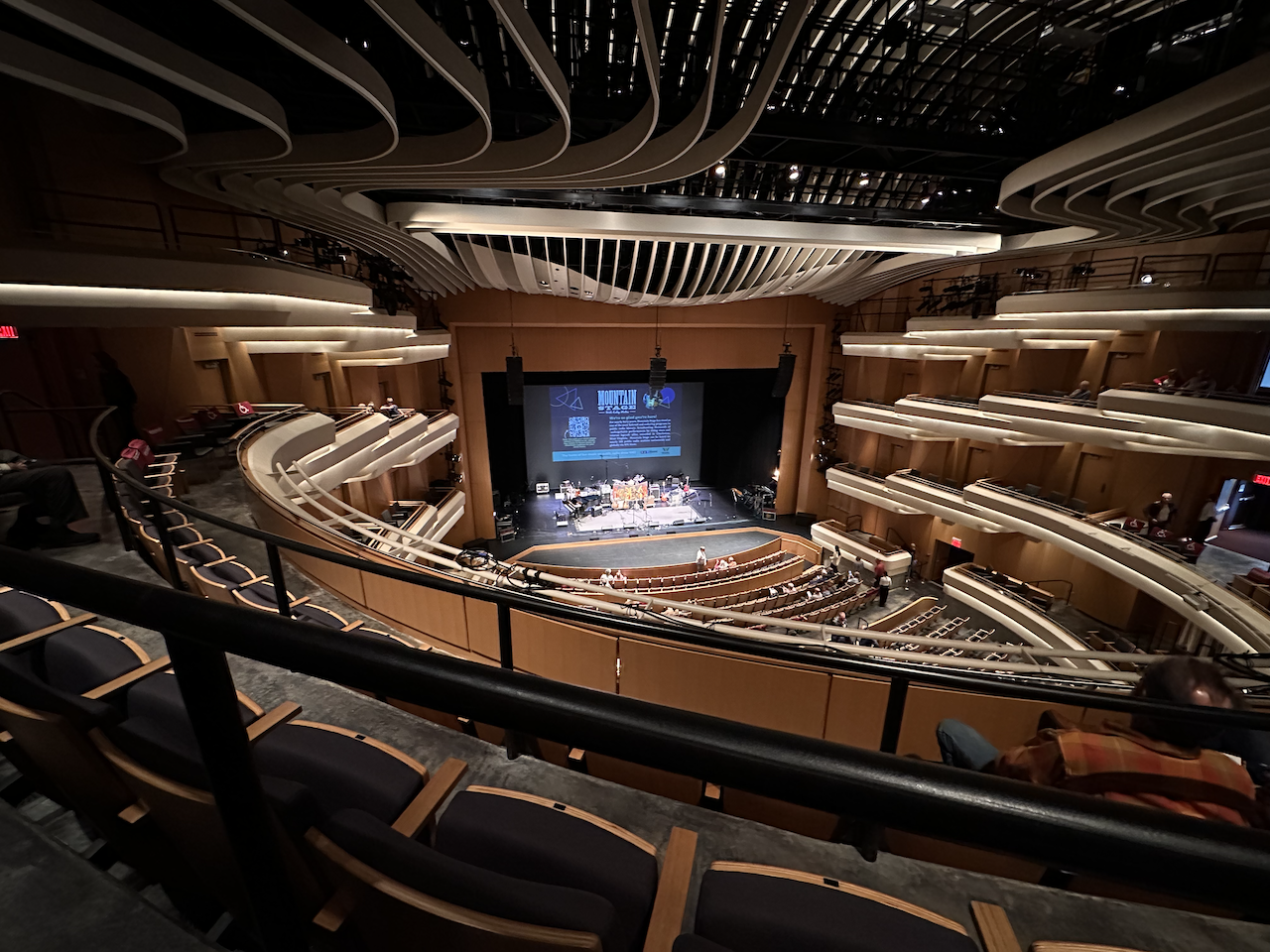 A mostly empty, modern auditorium with musical instruments set up on the stage. The picture has been taken from the balcony. Small box seats are visible to either side. A screen on stage promotes details of the NPR show Mountain Stage